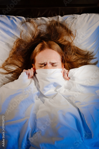 View top. a woman lies in bed under a white blanket and afraid, frightened. 