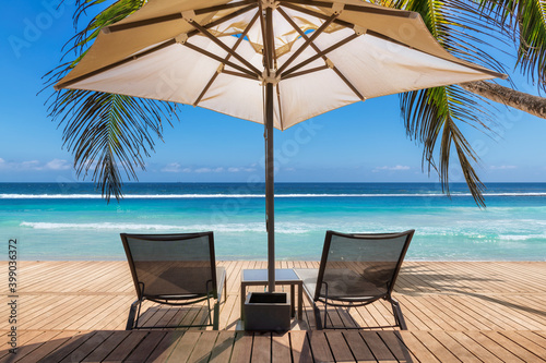 Tropical Sunny beach with umbrella and deckchairs on wooden floor  palm trees and the turquoise sea on Caribbean island 