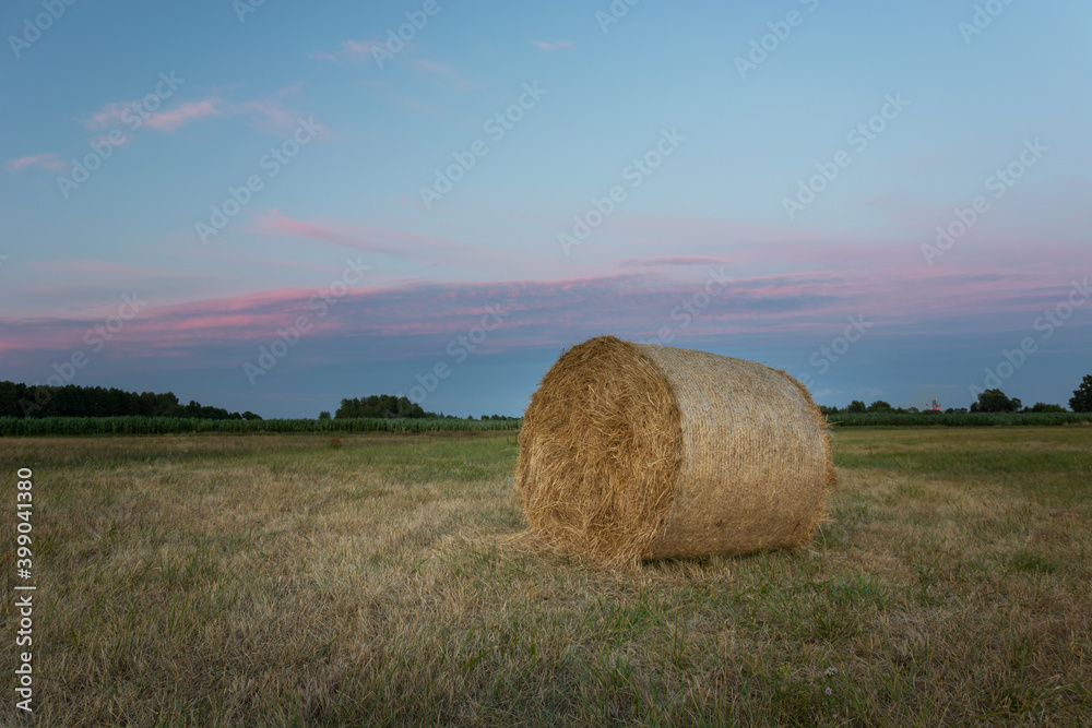 Round hay bale in the field and clouds after sunset