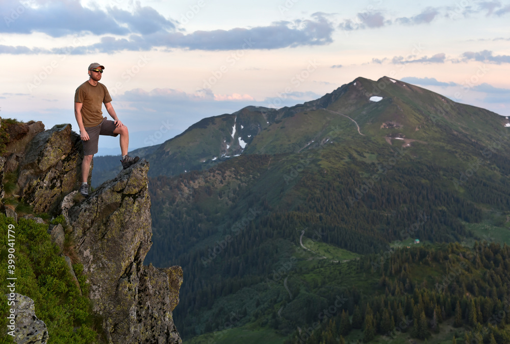 Man stands on the top of a rock against the background of Pip Ivan (Chornohora) mountain in the Ukrainian Carpathians at sunset