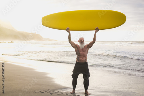 Hipster surfer senior man holding surf longboard on tropical beach - Joyful elderly lifestyle and extreme sport concept - Focus on face