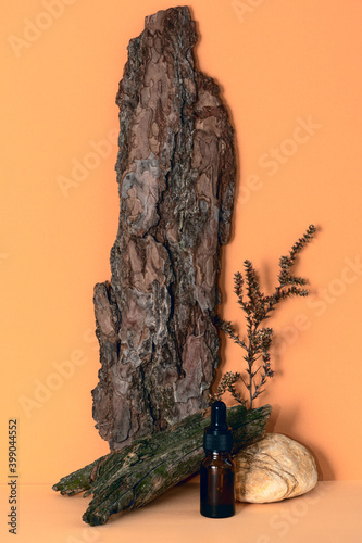 Brown cosmetic glass bottle with pipette, tree bark, stone, dried plant on beige background. Trend of natural materials and environmental friendliness. Wabi sabi concept.