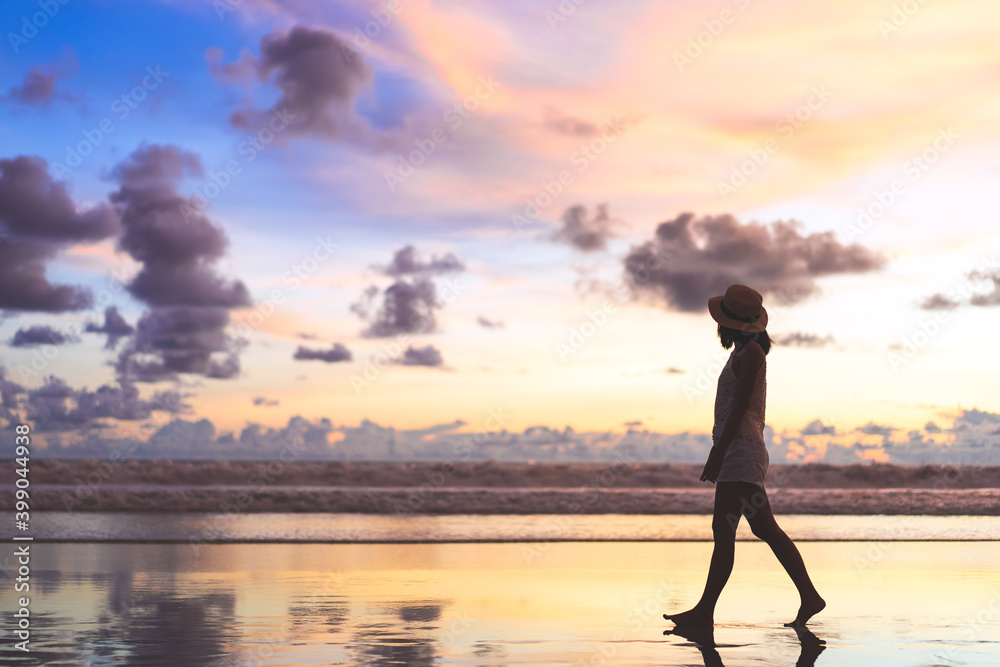 Rear view of young adult tourist asian woman walking relax on beach sand with beautiful dramatic sunset sky