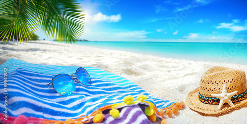 Summer background, concept beach vacation. Blue striped towel, Sunglasses with blue sky reflection,straw beach hat, palm leaves on background white sand and turquoise ocean. Island in Maldives.