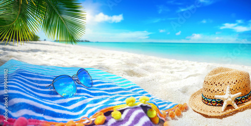 Fototapeta Naklejka Na Ścianę i Meble -  Summer background, concept beach vacation. Blue striped towel, Sunglasses with blue sky reflection,straw beach hat, palm leaves on  background white sand and turquoise ocean. Island in Maldives.
