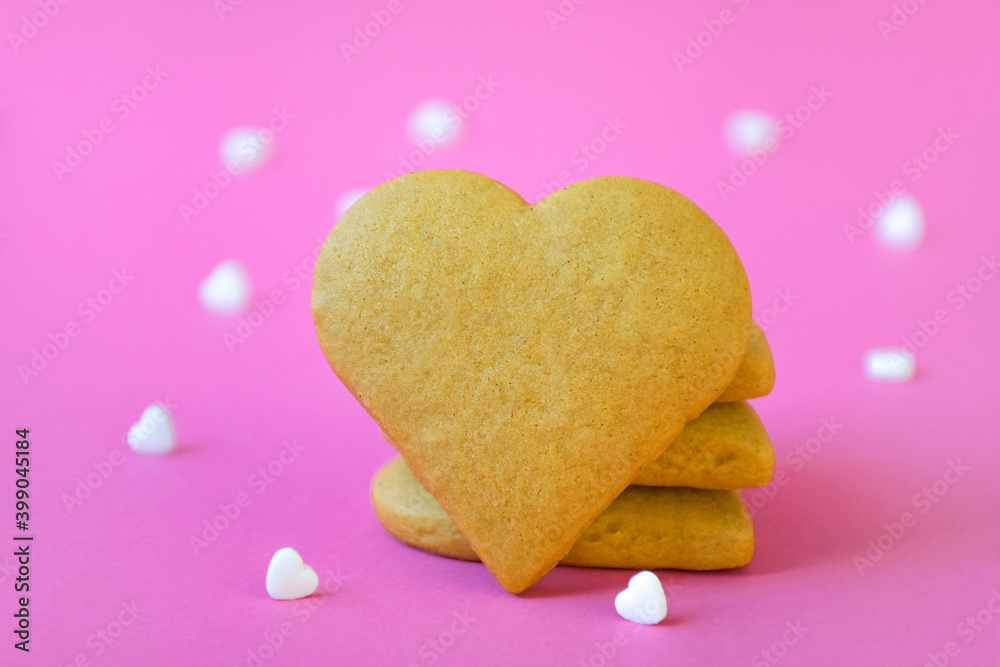 Stack of sugar cookies, heart shape biscuit with free place for text, many white heart shape candy confetti on pastel pink background. Freshly baked homemade bakery, pastry for teatime. Copy space.