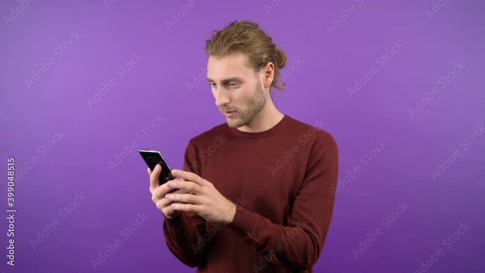 portrait of shocked surprised long-haired man browsing browser. Man on an isolated purple background. 4K portrait of shocked surprised long-haired man browsing browser. Man on an isolated purple background. 4K