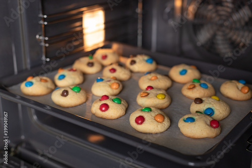 Baking tray with fresh cookies in oven. Delicious cookies with color sweets for children. soft focus
