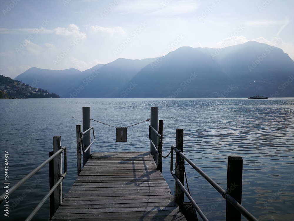 Wooden pier in the Lugano lake, Sitzerland with mountains in the background