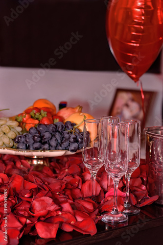 Empty wine glasses on a table covered with rose petals, with fruit and a balloon