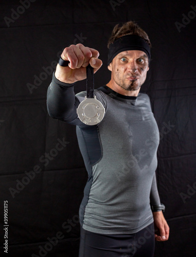 Handsome man in sportswear is insanely rejoicing at the received silver medal in the studio on a black background