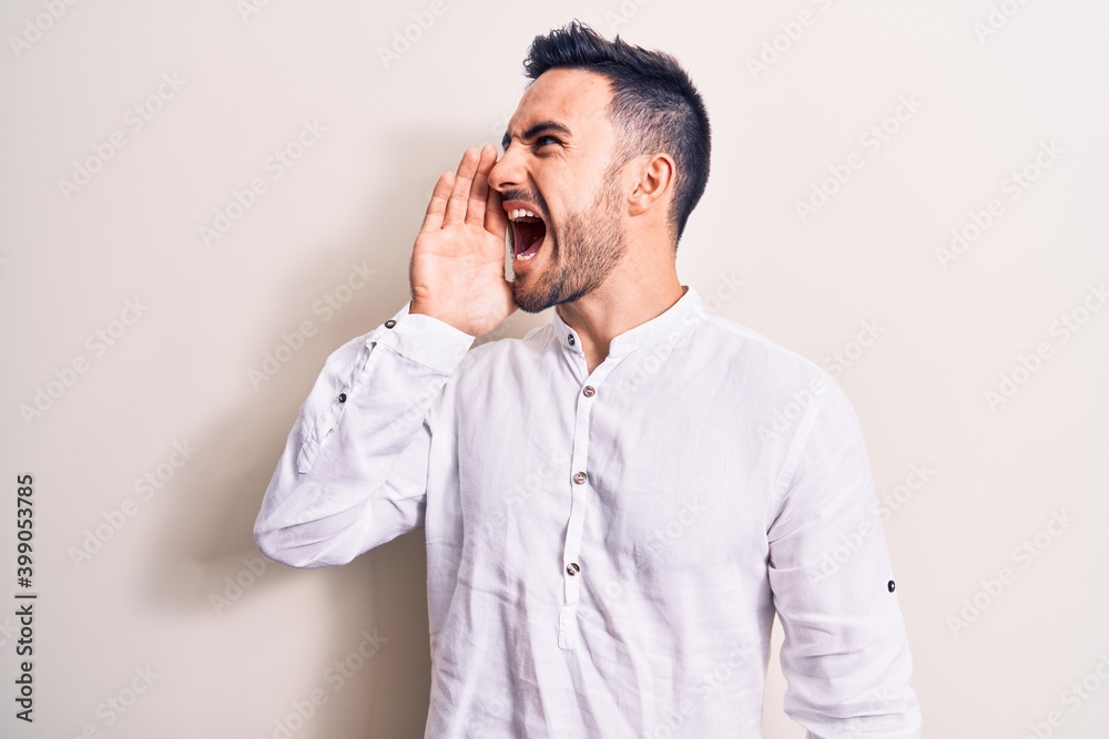 Young handsome man with beard wearing casual t-shirt standing over white background shouting and screaming loud to side with hand on mouth. Communication concept. Young handsome man with beard wearing casual t-shirt standing over white background shouting and screaming loud to side with hand on mouth. Communication concept.