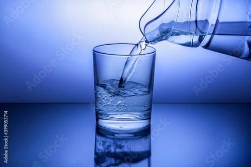 Pouring water from jug into glass on blue background