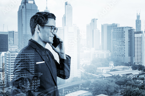 Prosperous handsome entrepreneur in suit and glasses pensively talking phone and looking on Kuala Lumpur cityscape. The concept of problem solving consulting . KL skyscrapers. Double exposure. photo