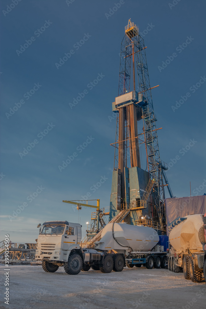Obraz premium In the background, a drilling rig in the northern oil and gas field. In the foreground is a grouting technique for cementing a casing in a well