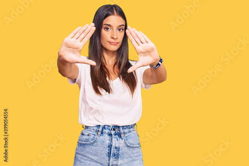Young hispanic woman wearing casual white tshirt doing frame using hands palms and fingers, camera perspective