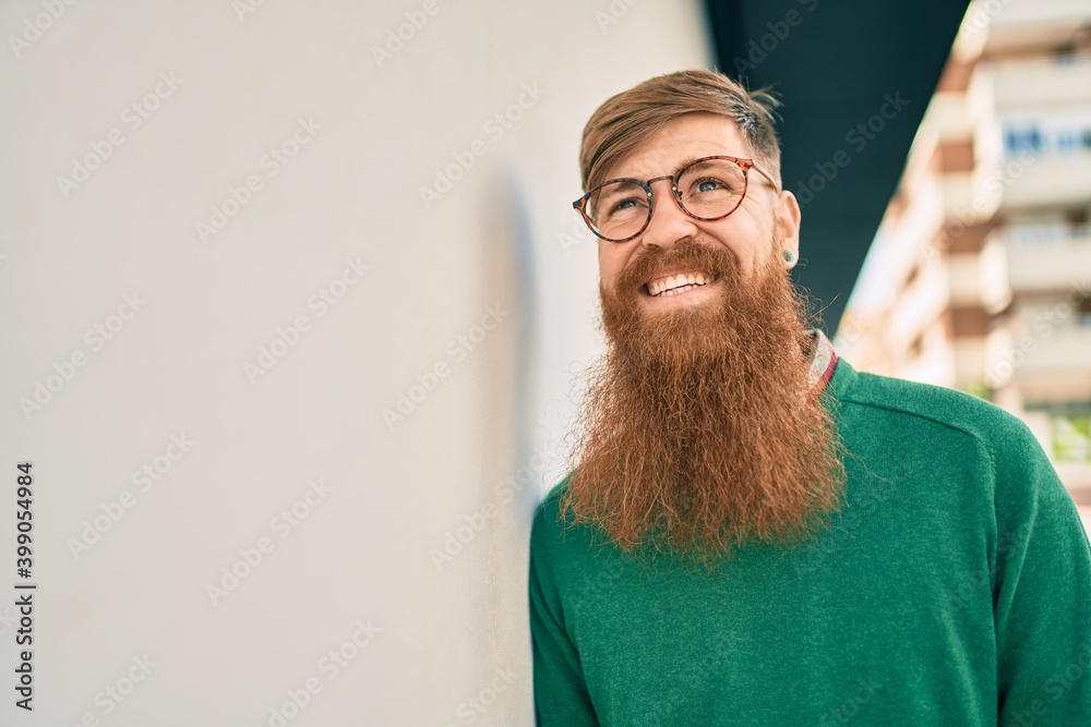 Young irish man with redhead beard smiling happy leaning on the wall at the city. - obrazy, fototapety, plakaty 