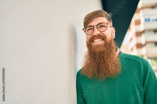 Young irish man with redhead beard smiling happy leaning on the wall at the city.