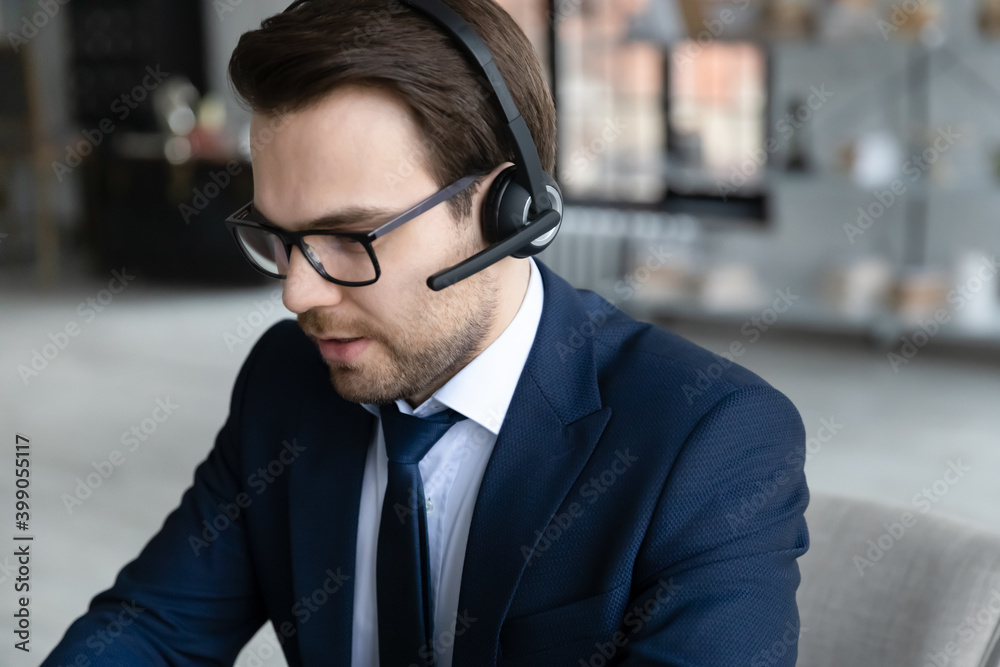 Close up confident businessman wearing glasses and headset consulting client online, focused support helpline service operator talking, executive making video call to partner, engaged in conference
