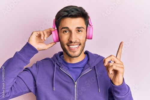 Young handsome man listening to music using headphones smiling happy pointing with hand and finger to the side