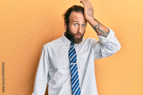 Handsome man with beard and long hair wearing business clothes surprised with hand on head for mistake, remember error. forgot, bad memory concept.