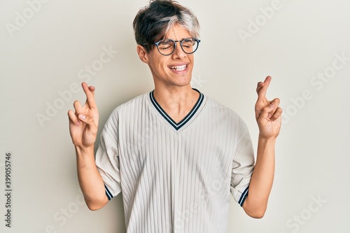 Young hispanic man wearing casual clothes and glasses gesturing finger crossed smiling with hope and eyes closed. luck and superstitious concept.