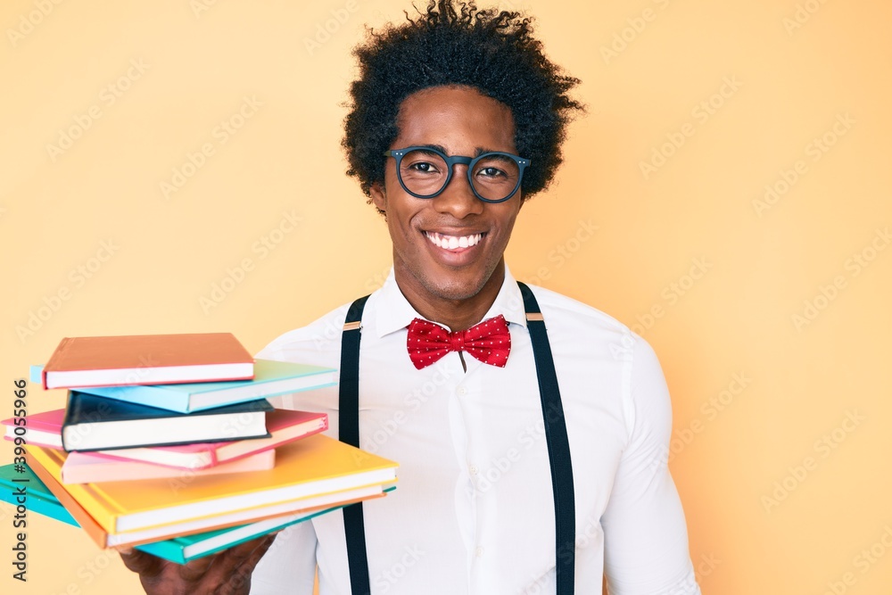Handsome african american nerd man with afro hair holding books looking positive and happy standing and smiling with a confident smile showing teeth Handsome african american nerd man with afro hair holding books looking positive and happy standing and smiling with a confident smile showing teeth