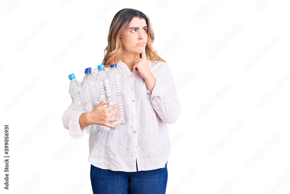 Young caucasian woman holding recycling plastic bottles serious face thinking about question with hand on chin, thoughtful about confusing idea Young caucasian woman holding recycling plastic bottles serious face thinking about question with hand on chin, thoughtful about confusing idea