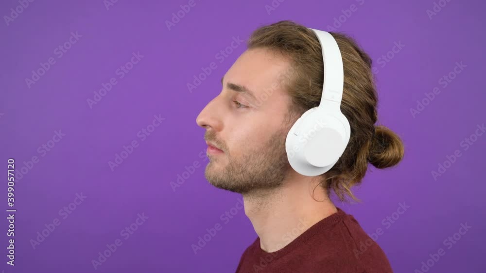 close-up portrait of a young dancing man wearing large white headphones. Isolated on purple background. 4K close-up portrait of a young dancing man wearing large white headphones. Isolated on purple background. 4K