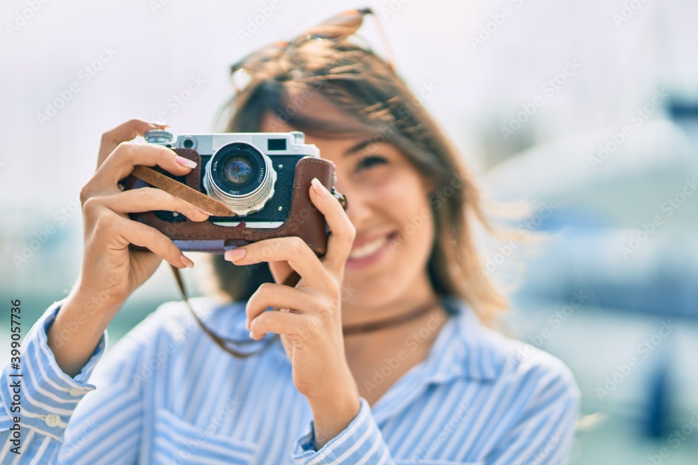 Young hispanic tourist woman smiling happy using vintage camera at the port.