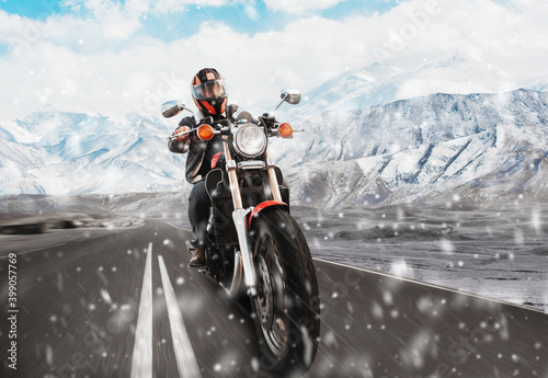 Motorcycle driver rides on the highway in the snow mountains. Snow is falling. front view