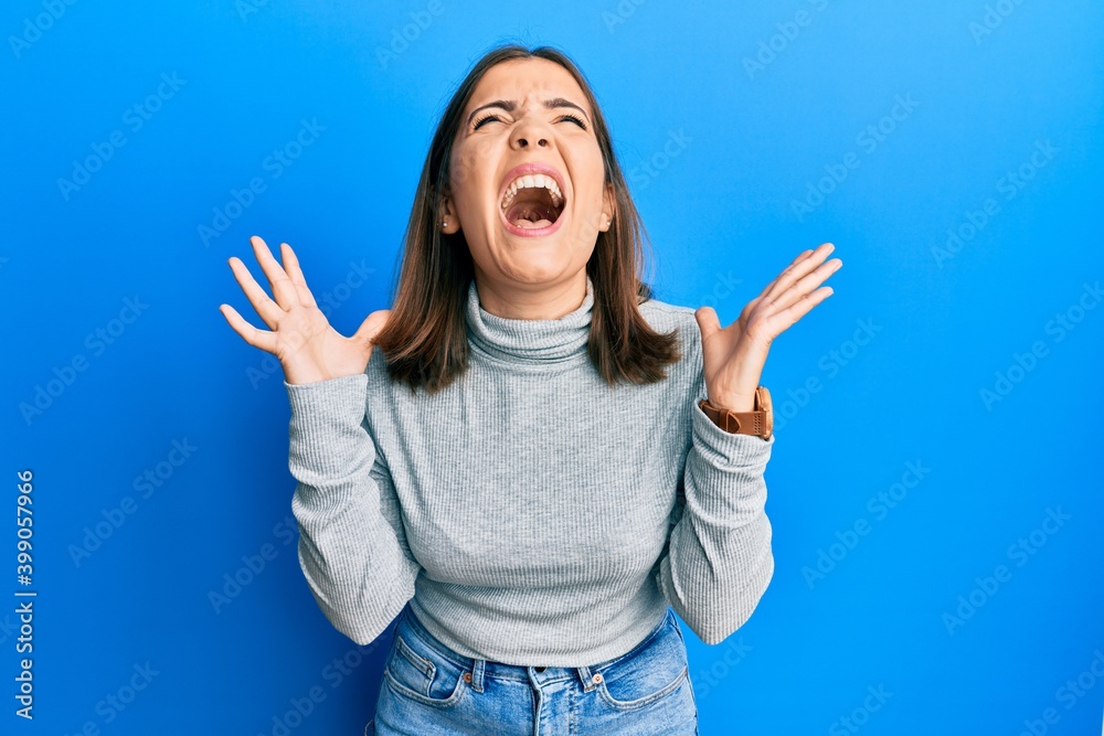 Young beautiful woman wearing casual turtleneck sweater celebrating mad and crazy for success with arms raised and closed eyes screaming excited. winner concept Young beautiful woman wearing casual turtleneck sweater celebrating mad and crazy for success with arms raised and closed eyes screaming excited. winner concept