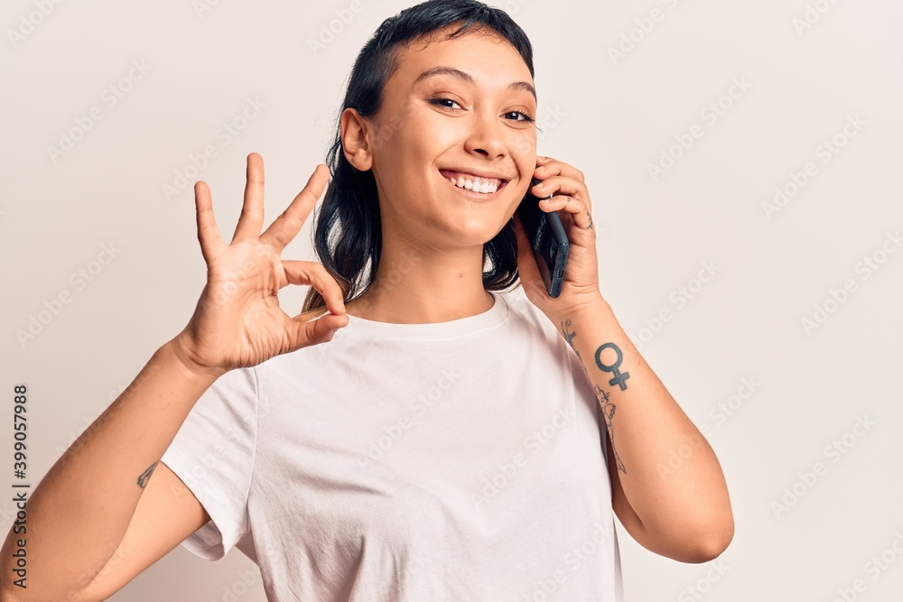 Young woman having conversation talking on the smartphone doing ok sign with fingers, smiling friendly gesturing excellent symbol Young woman having conversation talking on the smartphone doing ok sign with fingers, smiling friendly gesturing excellent symbol