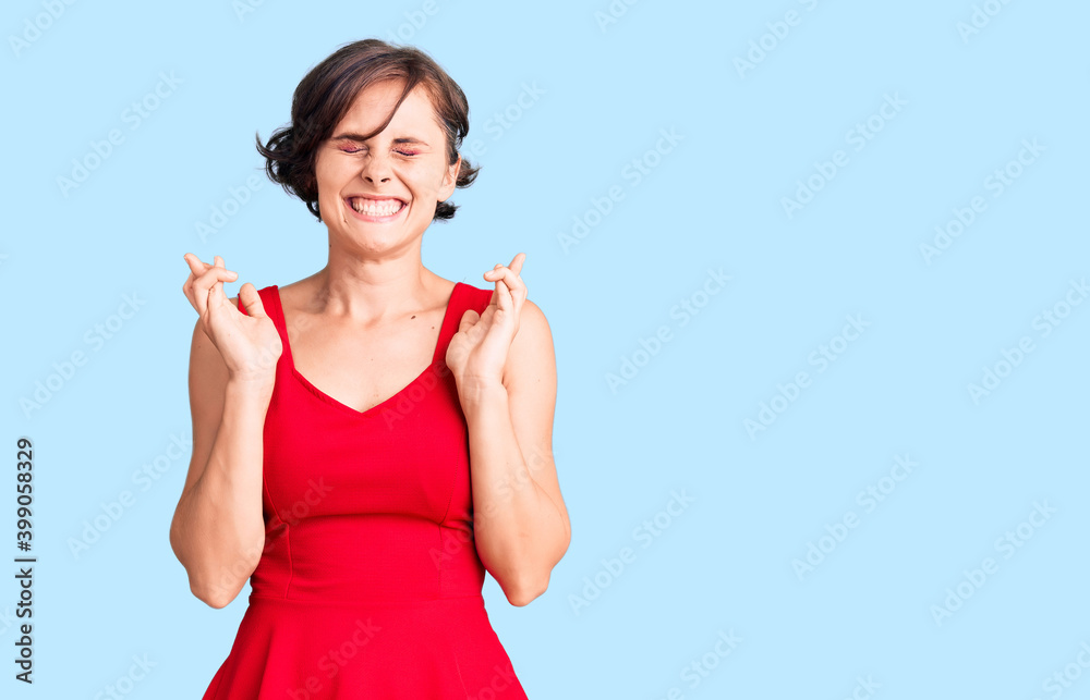 Beautiful young woman with short hair wearing casual style with sleeveless shirt gesturing finger crossed smiling with hope and eyes closed. luck and superstitious concept. Beautiful young woman with short hair wearing casual style with sleeveless shirt gesturing finger crossed smiling with hope and eyes closed. luck and superstitious concept.