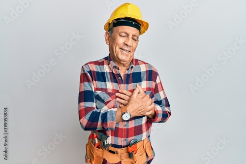 Senior hispanic man wearing handyman uniform smiling with hands on chest with closed eyes and grateful gesture on face. health concept.