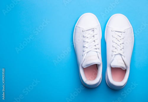 Pair of stylish sport shoes on blue background. Top view of white sneakers on color background with place for text