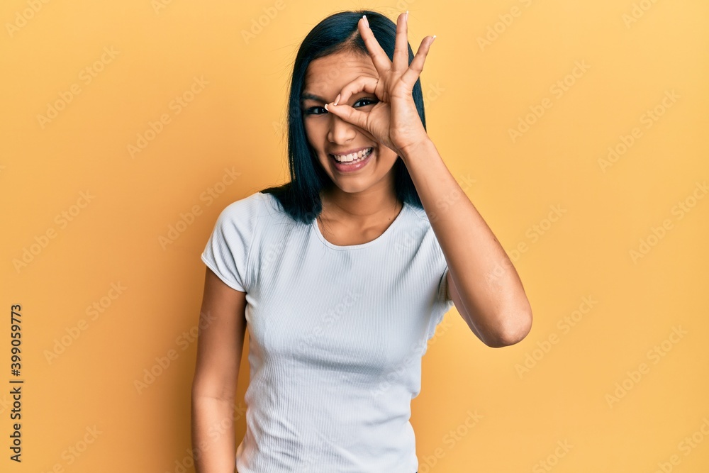 Beautiful hispanic woman wearing casual white tshirt doing ok gesture with hand smiling, eye looking through fingers with happy face. Beautiful hispanic woman wearing casual white tshirt doing ok gesture with hand smiling, eye looking through fingers with happy face.