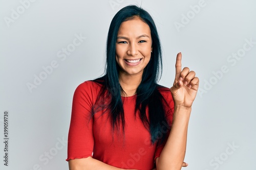 Beautiful hispanic woman wearing casual clothes smiling with an idea or question pointing finger up with happy face  number one
