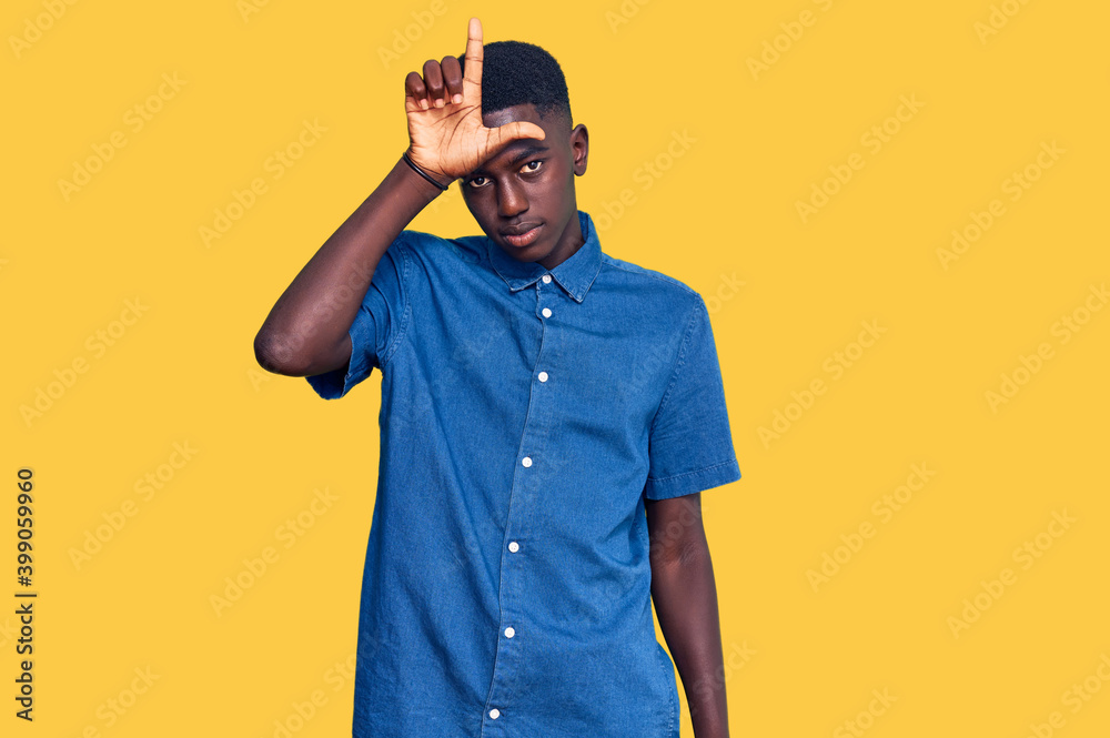 Young african american man wearing casual clothes making fun of people with fingers on forehead doing loser gesture mocking and insulting. Young african american man wearing casual clothes making fun of people with fingers on forehead doing loser gesture mocking and insulting.