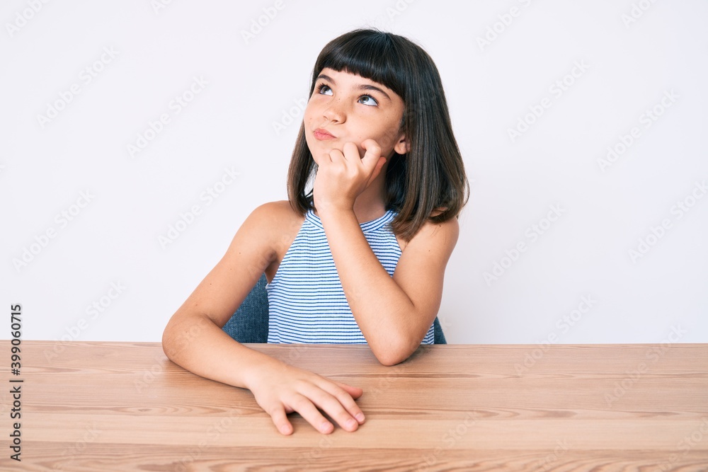 Young little girl with bang wearing casual clothes sitting on the table thinking concentrated about doubt with finger on chin and looking up wondering Young little girl with bang wearing casual clothes sitting on the table thinking concentrated about doubt with finger on chin and looking up wondering