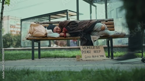 Homeless person sleeping on a park bench, indifferent people walking by