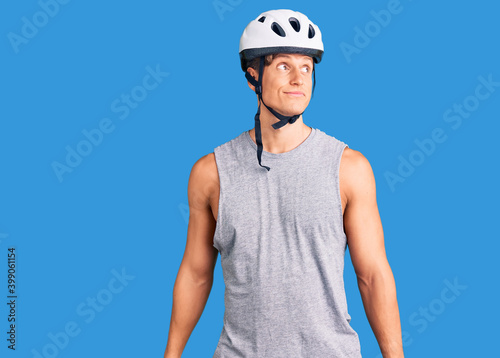 Young handsome man wearing bike helmet smiling looking to the side and staring away thinking.