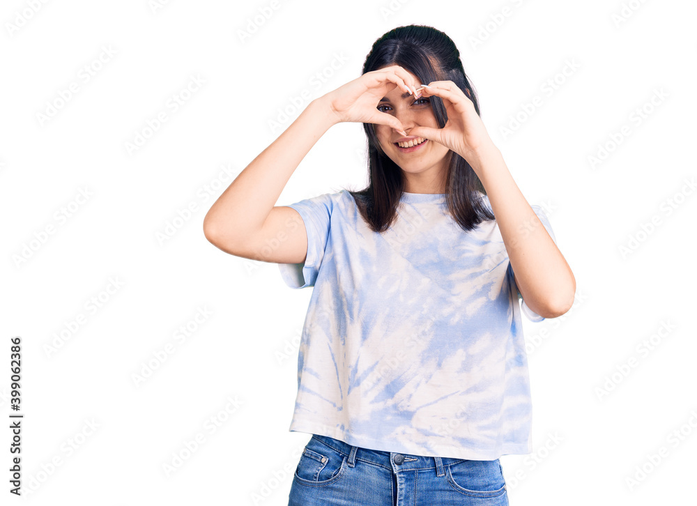 Young beautiful girl wearing casual t shirt doing heart shape with hand and fingers smiling looking through sign Young beautiful girl wearing casual t shirt doing heart shape with hand and fingers smiling looking through sign