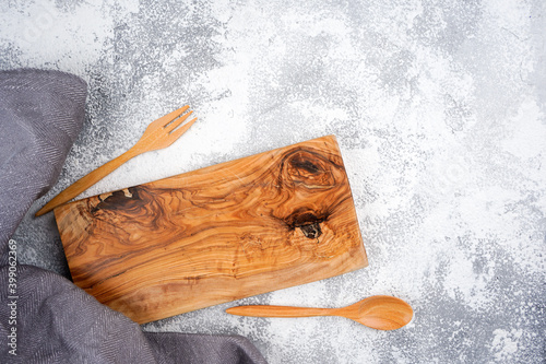 Wooden cutting board, cutlery, gray kitchen towel frame on light concrete background. Cooking, recipe, menu concept. Top view, flat lay, copy space