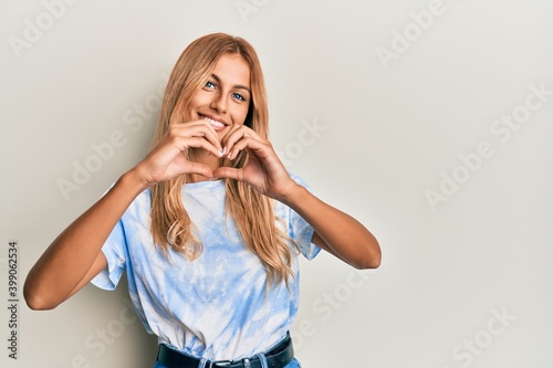 Beautiful blonde young woman wearing tye die tshirt smiling in love doing heart symbol shape with hands. romantic concept. photo