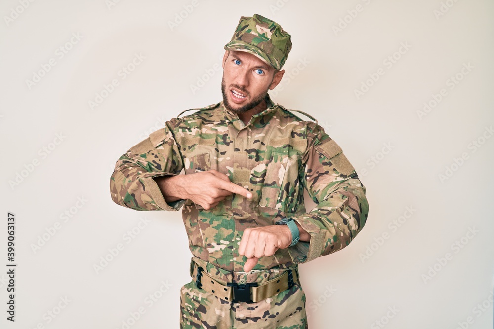 Young caucasian man wearing camouflage army uniform in hurry pointing to watch time, impatience, upset and angry for deadline delay Young caucasian man wearing camouflage army uniform in hurry pointing to watch time, impatience, upset and angry for deadline delay
