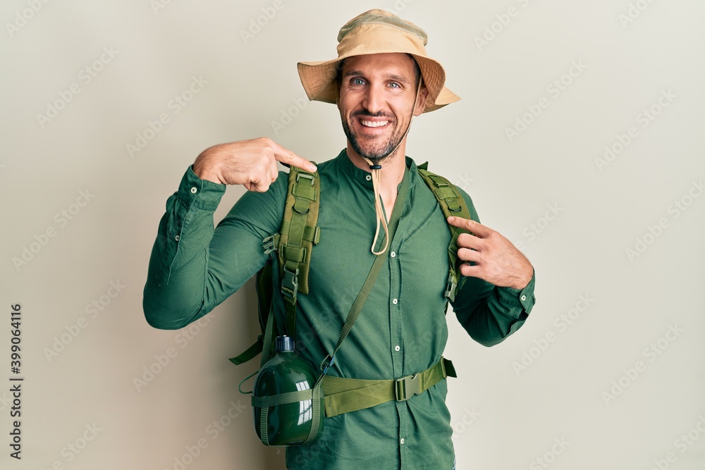 Handsome man with beard wearing explorer hat and backpack looking confident with smile on face, pointing oneself with fingers proud and happy. Handsome man with beard wearing explorer hat and backpack looking confident with smile on face, pointing oneself with fingers proud and happy.