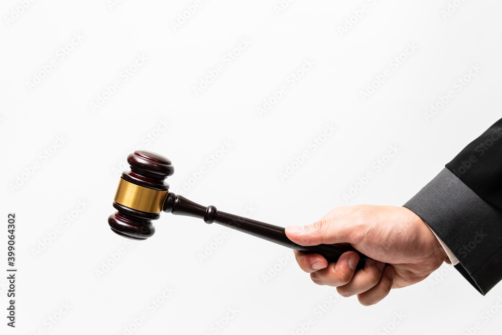 Judge or lawyer in with white shirt, gray suit and blacke robe is using his hand to hold wooden gavel against the white background. Judge or lawyer in with white shirt, gray suit and blacke robe is using his hand to hold wooden gavel against the white background.