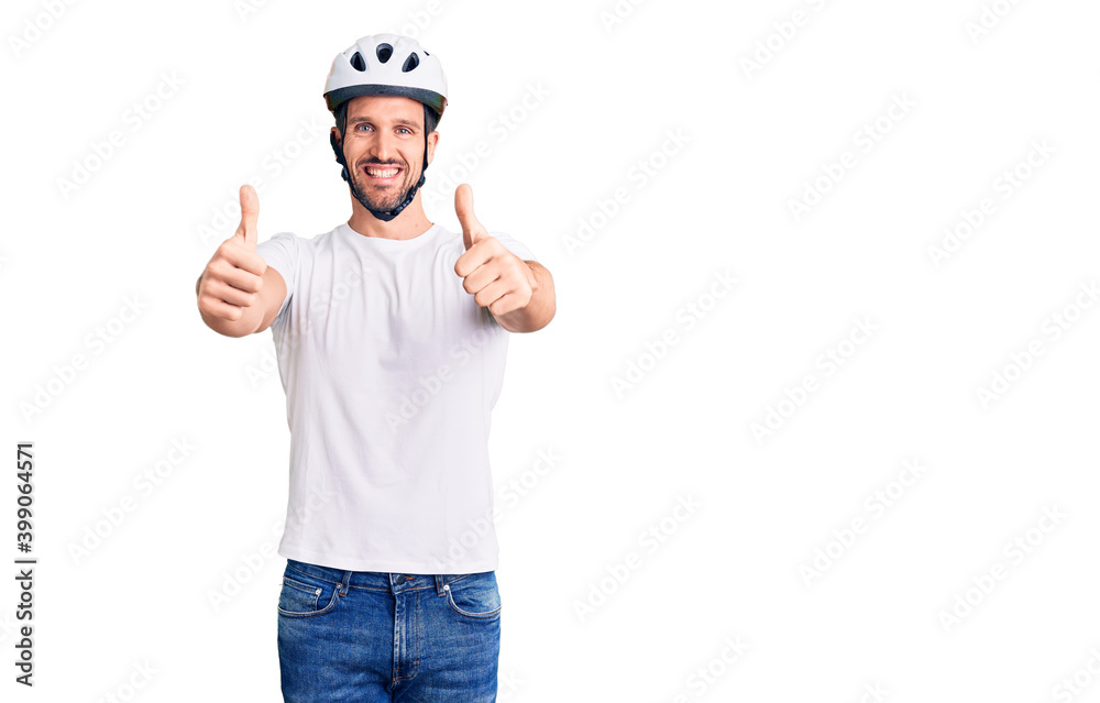Young handsome man wearing bike helmet approving doing positive gesture with hand, thumbs up smiling and happy for success. winner gesture. Young handsome man wearing bike helmet approving doing positive gesture with hand, thumbs up smiling and happy for success. winner gesture.