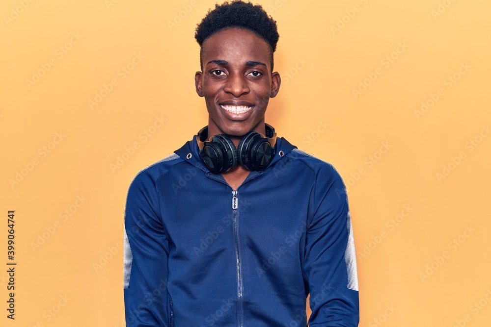 Obraz premium Young african american man wearing sportswear and headphones with a happy and cool smile on face. lucky person.